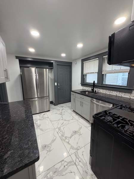 Modern kitchen with stainless steel appliances, white cabinets, black countertops, and marble-pattern tile floor.