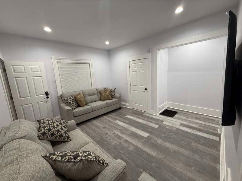 Bright living room with gray sofas, white walls, recessed lights, and gray patterned flooring.