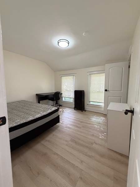 Small bright bedroom with bed, desk, two windows, and light wood floor