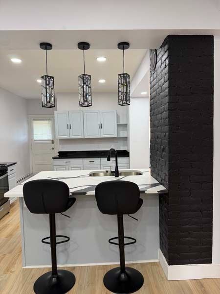 Modern white kitchen with black bar stools, pendant lights, and a dark brick column