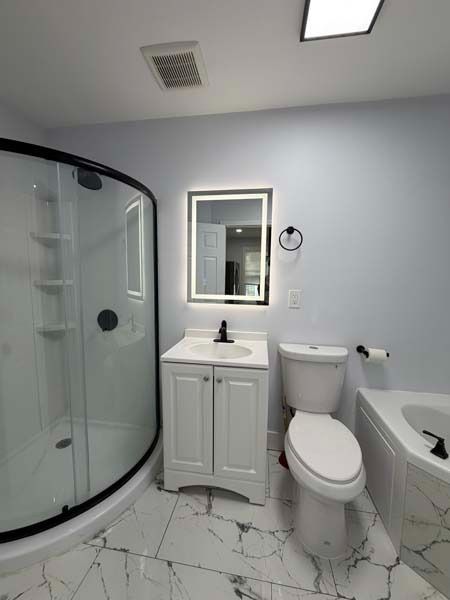 Modern bathroom with glass shower, vanity sink, toilet, and marble tile floor