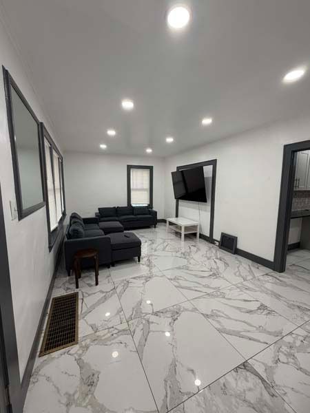 Modern living room with gray sofas, wall-mounted TV, and glossy white marble-pattern floor.