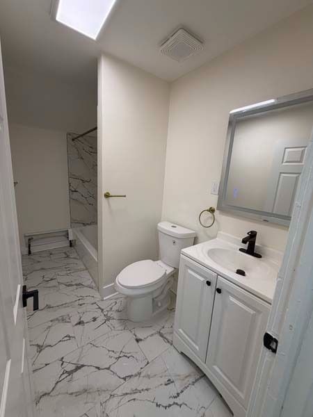Small white bathroom with marble tile floor, vanity sink, toilet, and walk-in shower.