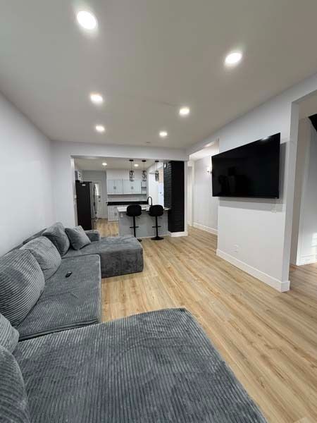 Modern living room with gray sectional, wall-mounted TV, and open kitchen with bar stools