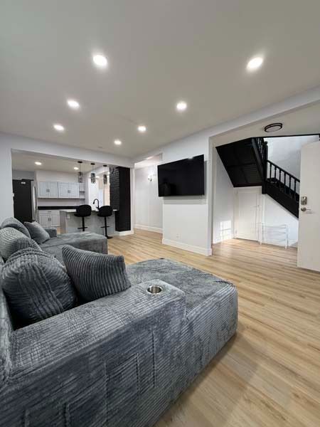 Modern open-plan living room with gray sectional, wall-mounted TV, wood floors, and staircase