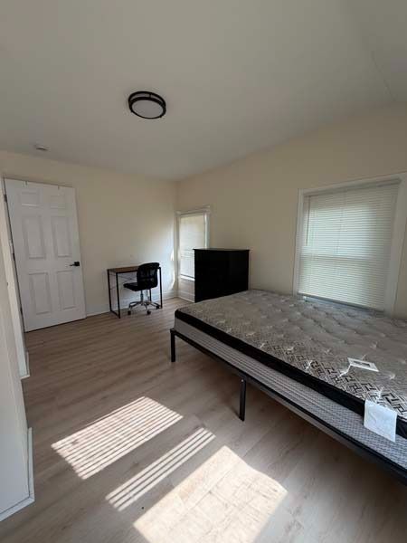 Empty bedroom with a bed, TV, desk, and sunlight on the floor