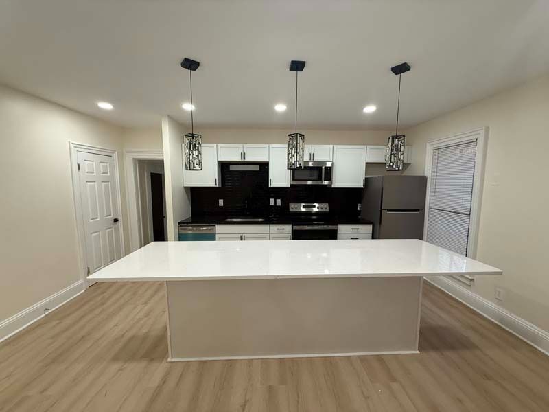 Modern kitchen with large white island, black cabinets, pendant lights, and stainless steel refrigerator