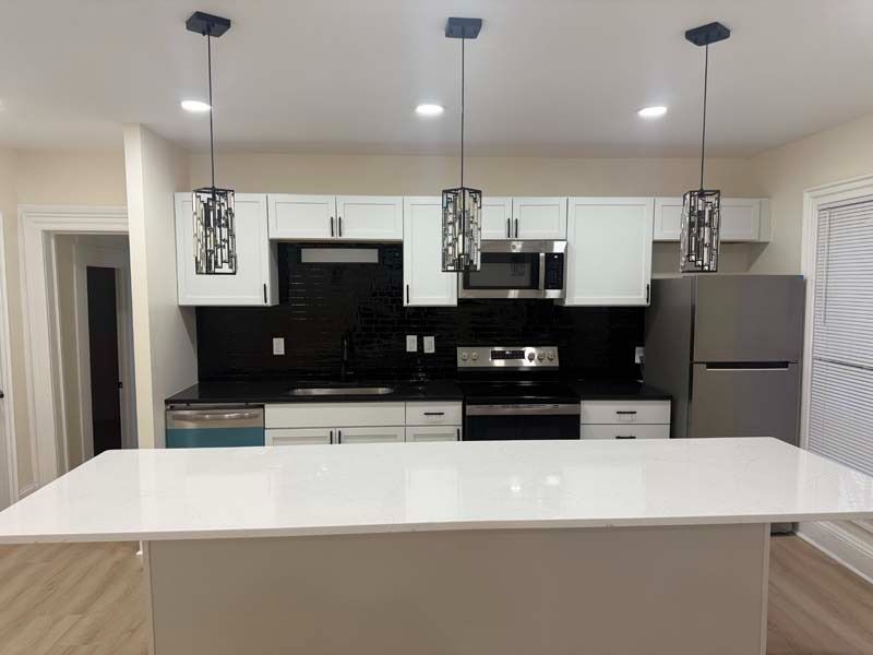 Modern kitchen with white island, black backsplash, stainless appliances, and pendant lights