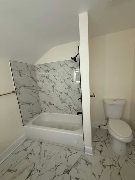 Small bathroom with marble-pattern tile, bathtub, half wall, and toilet on the right.