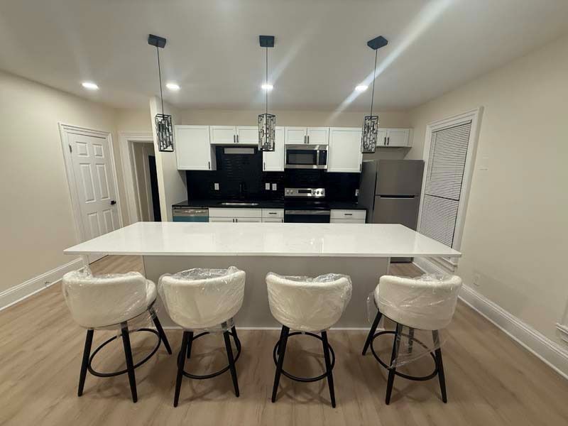 Modern kitchen with white island, four stools, black cabinets, and stainless steel appliances