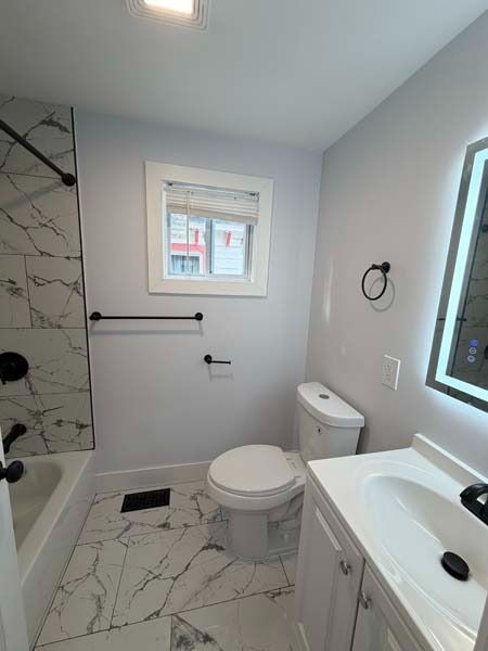 Modern white bathroom with tub, toilet, sink, marble tile, and window