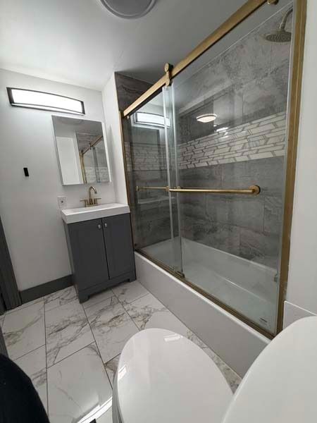 Modern bathroom with glass shower, gray vanity, mirror, and white marble floor tiles