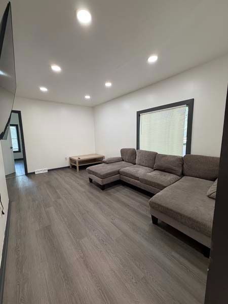 Modern living room with gray sectional sofa, wood floors, recessed lights, and a small bench by the wall