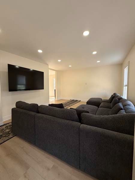 Modern living room with dark sectional sofa, wall-mounted TV, recessed lights, and large windows