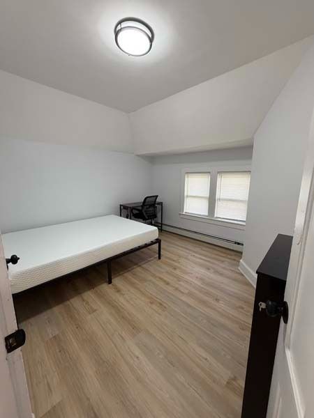 Small empty bedroom with a bed, two windows, white walls, and wood flooring.