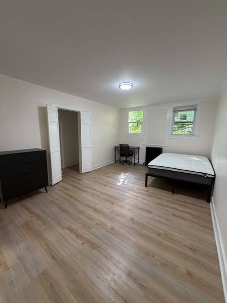 Minimal bedroom with bed, dresser, desk, and two small windows on light wood flooring