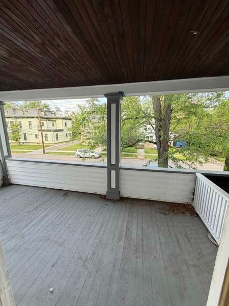 Covered porch with gray floor, white railing, and view of a street and houses through open sides