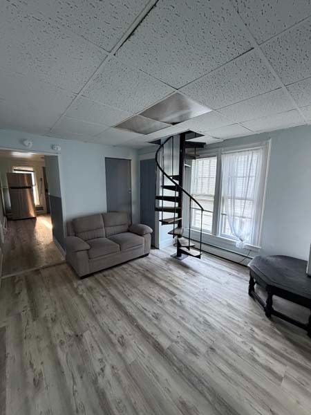 Small living room with gray sofa, spiral loft stairs, and bright window with sheer curtains