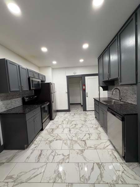Modern kitchen with dark cabinets, white marble-pattern floor, and recessed ceiling lights