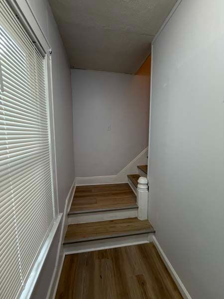 Narrow hallway with white walls, wood floor, and a small stairway leading up.