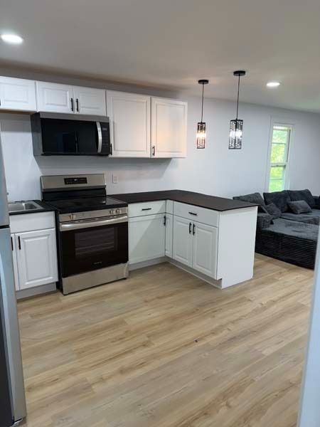 Bright kitchen with white cabinets, stainless steel appliances, dark counters, and light wood flooring.