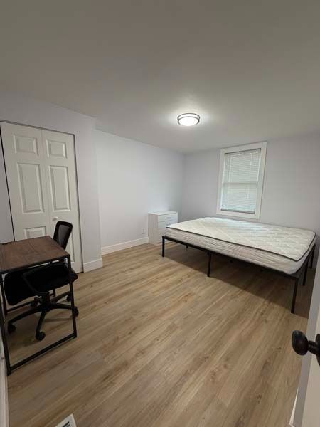 Small bedroom with a bed, desk, chair, and white walls, viewed from the doorway.