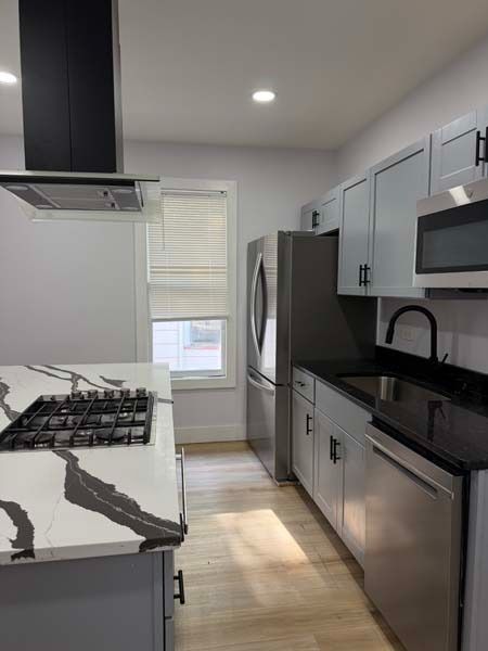 Modern galley kitchen with black countertops, stainless appliances, white cabinets, and a window at the end.