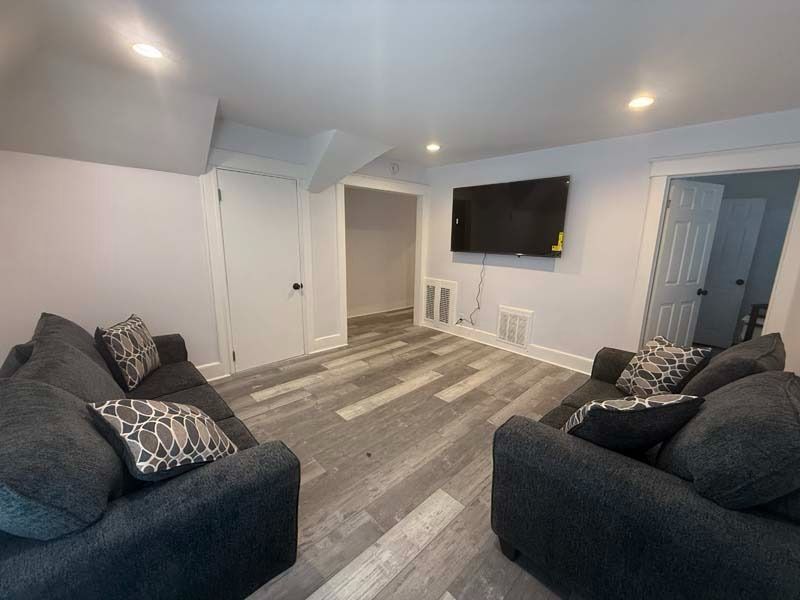 Small living room with gray sofas, wall-mounted TV, and gray wood flooring.