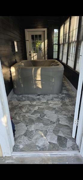 Small enclosed porch with stone floor and a large cardboard box centered inside, lit by window light.