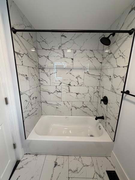 Walk-in shower with white marble-look tile, black fixtures, and a bathtub inside.