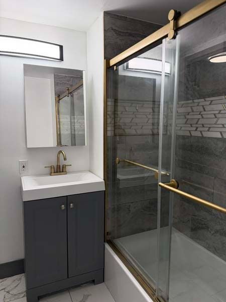 Modern bathroom with dark vanity, mirror, and glass-enclosed shower with brass trim.