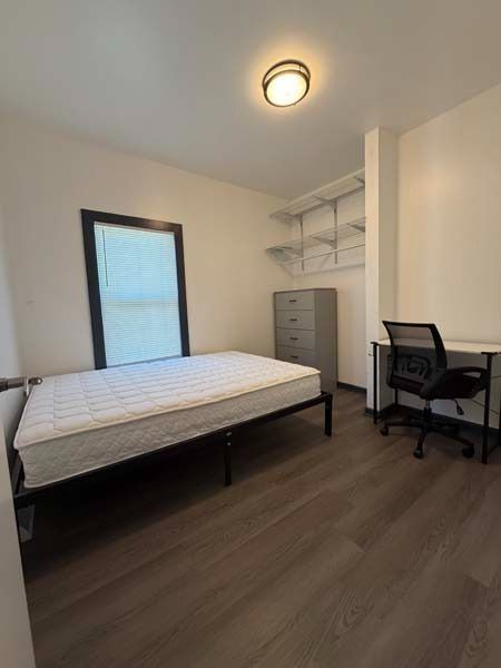 Small bedroom with bed, desk, chair, dresser, and wall shelves in neutral tones