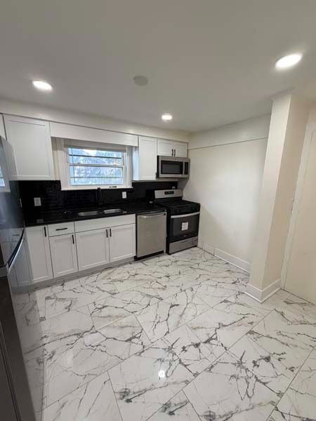 Modern white kitchen with black countertops, stainless appliances, and marble-patterned floor tiles