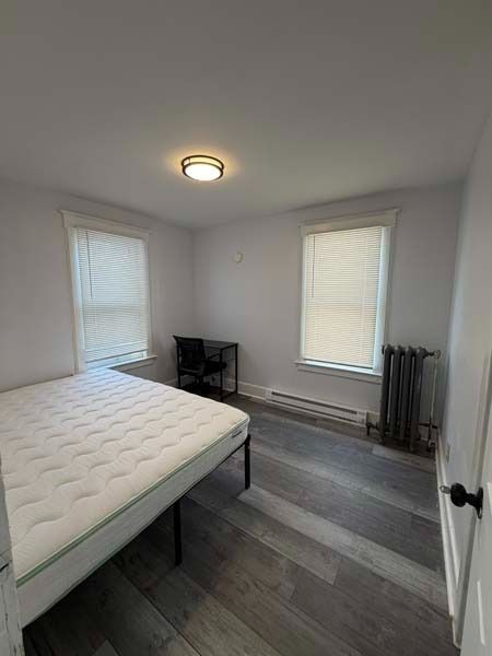 Small bedroom with a bed, two windows, gray walls, and a radiator near the corner.