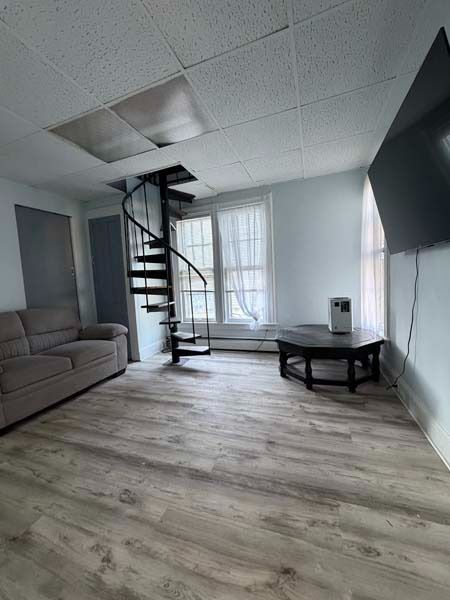 Small living room with spiral staircase, gray sofa, coffee table, and bright windowed wall