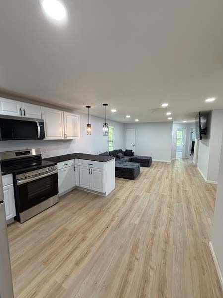 Open-plan kitchen and living room with light wood floors, white cabinets, gray sofa, and recessed ceiling lights