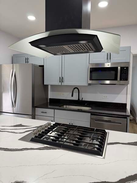 Modern white kitchen with stainless appliances, island cooktop, and black range hood