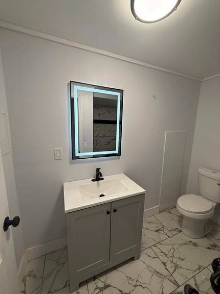 Modern bathroom with gray vanity, lit mirror, white toilet, and marble-pattern tile floor.