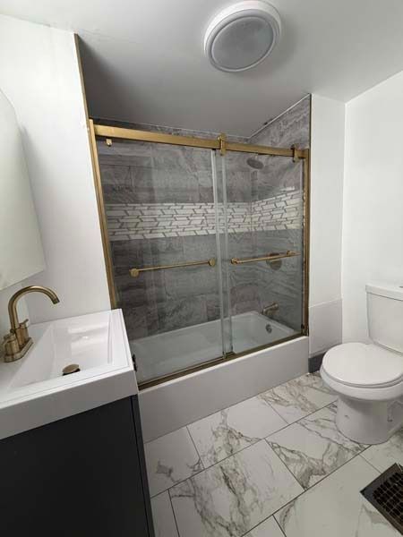 Modern bathroom with marble tile, glass shower, sink, and toilet