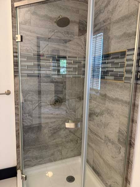 Glass shower stall with gray tile walls, chrome showerhead, and white base tiles