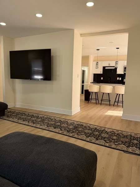 Modern living room with wall-mounted TV, dark sofa, patterned rug, and view into a kitchen with bar stools
