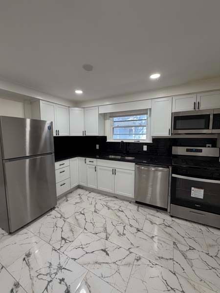 Modern white kitchen with stainless steel appliances, black backsplash, and marble-patterned tile floor
