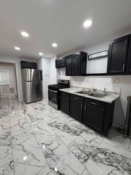 Modern kitchen with stainless steel appliances, dark cabinets, and glossy white marble-look tile floor