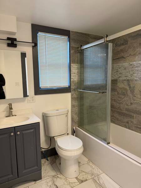 Small bathroom with toilet, vanity, glass shower, and window blinds.
