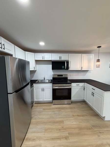 Modern white kitchen with stainless steel appliances, dark countertops, and light wood flooring.