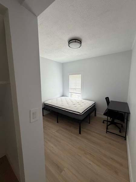 Small bedroom with a bed, desk, and chair, white walls, wood floor, and a window with blinds