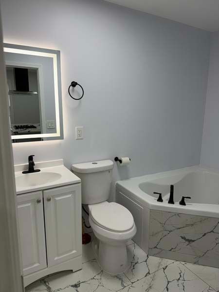 Bright bathroom with white vanity, toilet, and marble tub with black fixtures