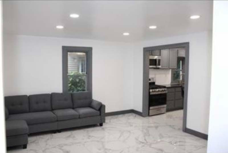 Modern living room with gray sofa, white tile floor, and open view into a kitchen
