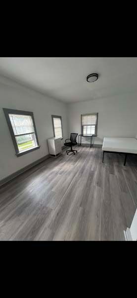 Empty bedroom with gray floors, white walls, two windows, a desk, and a bed