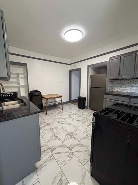 Small kitchen with gray cabinets, white marble-pattern floor, black stove, and round ceiling light.